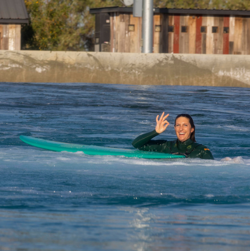 Photo of a person in the water waving while next to a surfboard