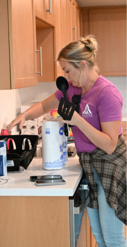 A woman in a pink Allgire Foundation t-shirt unboxing kitchen supplies