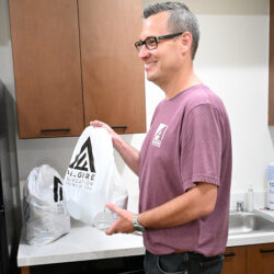 A man in a pink Allgire Foundation t-shirt holding a bag of supplies with the Allgire Foundation logo